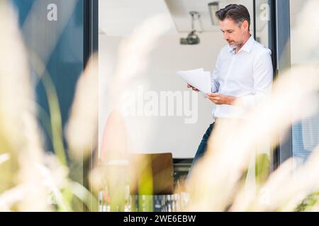 Mature businessman leaning on door and reading documents Stock Photo
