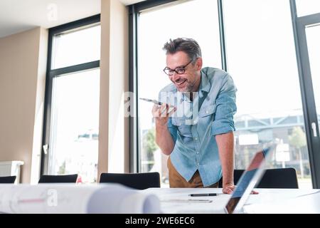 Happy architect discussing over blueprint on smart phone in office Stock Photo