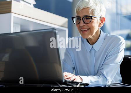 Happy businesswoman wearing eyeglasses and using laptop at office Stock Photo