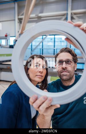 Colleagues analyzing circle shape machine part in workshop Stock Photo