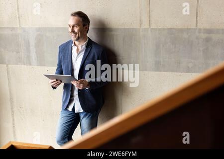 Happy businessman with tablet computer in front of wall Stock Photo