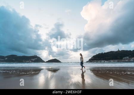 Young tourist walking on Playa de la Concha shore under cloudy sky Stock Photo