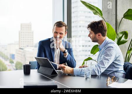 Smiling businessmen having discussion over tablet PC at office Stock Photo