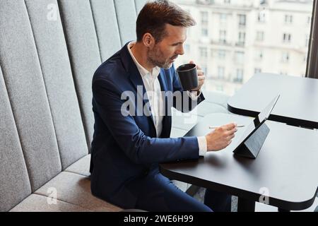 Businessman using tablet PC and drinking coffee in office Stock Photo