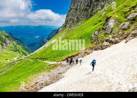 Group of hikers walking through snow on the trail from Busteni to the Omu Peak through Râul Valea Priponului valley, Bucegi Mountains, Romania Stock Photo