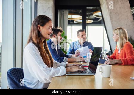 Smiling businesswoman using laptop near colleagues at office Stock Photo