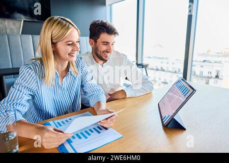 Happy businessman and businesswoman analyzing graphs on tablet PC at desk Stock Photo