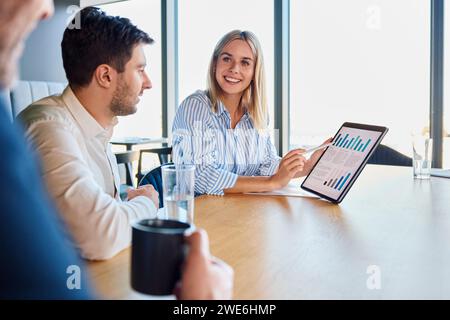 Happy young businesswoman discussing over graph with colleagues Stock Photo