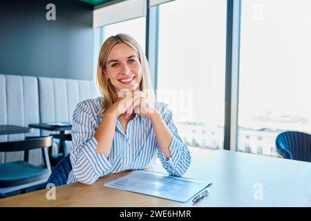 Smiling blond businesswoman sitting with graph at desk Stock Photo