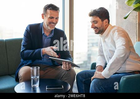 Happy businessmen discussing over tablet PC in office lobby Stock Photo