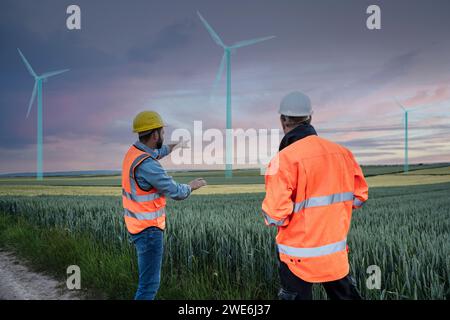Engineer pointing at digital wind turbine design standing with colleague in field Stock Photo