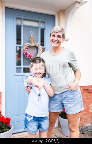 Happy woman with daughter showing keys standing in front of house Stock Photo