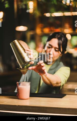 Bartender pouring cocktail drink in glass on bar counter Stock Photo