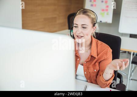 Young businesswoman wearing headset and having video conference in office Stock Photo