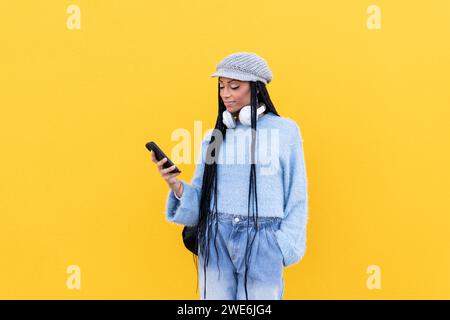 Woman using smart phone in front of yellow wall Stock Photo