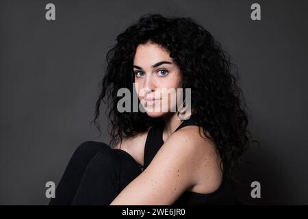 Curly haired beautiful woman sitting against gray background Stock Photo