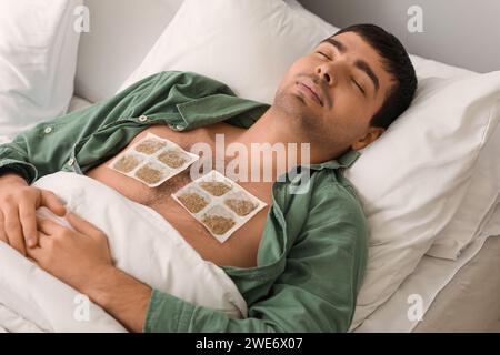 Ill young man with mustard plasters on his chest sleeping in bedroom Stock Photo