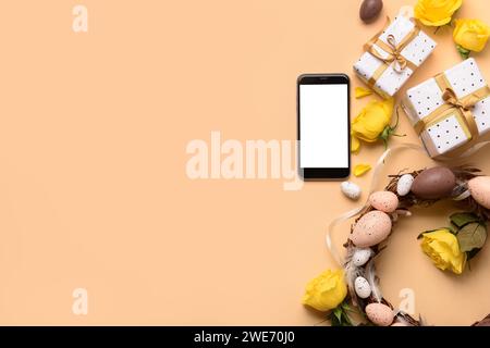 Composition with modern mobile phone, gifts and Easter wreath on color background Stock Photo