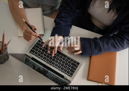 Top view of two women are discussing work, looking at a laptop computer screen, and working together in the office. Stock Photo