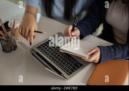 Close-up image of two female office employees are discussing on a project and working in the office together, taking note on a book and using laptop. Stock Photo