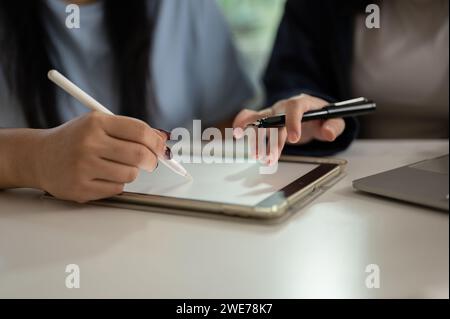 Cropped shot of two Asian women are discussing work and using a digital tablet to plan their project in the office together. people and technology con Stock Photo