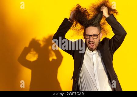 Portrait of stressed long-haired businessman pulling his hair out over yellow background Stock Photo