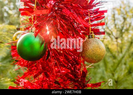 Green and gold Christmas ornaments and red tensile garland hanging on pine tree in local park in South Korea Stock Photo