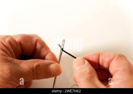 Woman threading a needle with a black thread isolated on white background and copy space Stock Photo