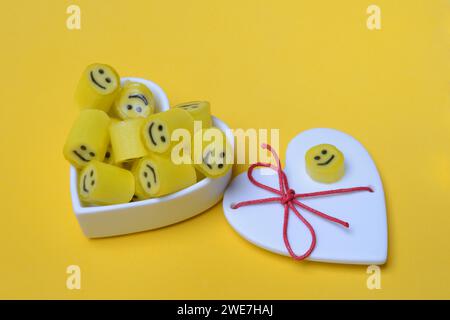 Yellow sweets with smiley in a heart-shaped bowl Stock Photo