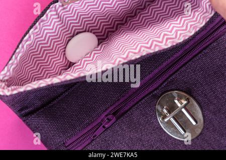 An Apple Air Tag lies in a purple clutch against a plain pink background Stock Photo