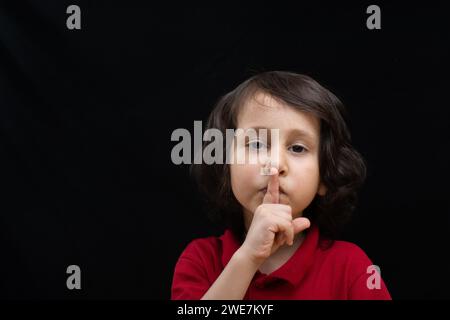 Cute kid put index finger over lips for quiet gesture Stock Photo