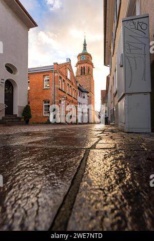 Damp cobblestones lead to the church tower between houses, graffiti on the wall in late light, Weil der Stadt, Germany Stock Photo