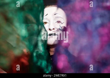 Dramatic close up portrait of mime performer looking at camera on stage in spotlight holding magic shimmering cloth, copy space Stock Photo