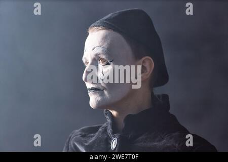 Dramatic headshot portrait of mime artist standing on stage in spotlight and looking away with sad face makeup, copy space Stock Photo