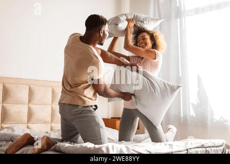 African American boyfriend and girlfriend having fun pillow fight indoor Stock Photo