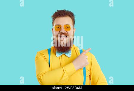 Optimistic funny happy man with yellow shirt and glasses points his finger at empty space for advertising. Stock Photo