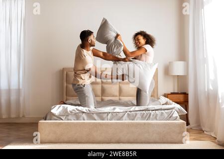 black husband and wife having fun fighting with pillows indoor Stock Photo