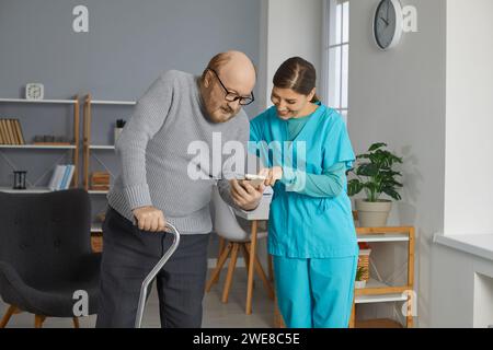 Senior man with walking stick showing young nurse some photos on his mobile phone Stock Photo