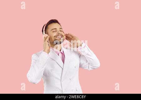 Happy young man enjoys his favorite music with modern headphones on pastel pink background. Stock Photo