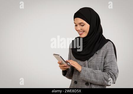 Engaged Muslim woman using smartphone and smiling Stock Photo