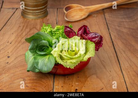 Four salads in a cup on an antique wooden table: green grumolo chicory, radicchio from Chioggia, radicchio from Castelfranco and curly salad. Stock Photo