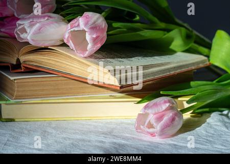 Bouquet of pink tulips and a stack of three books on a white sheet. Stock Photo