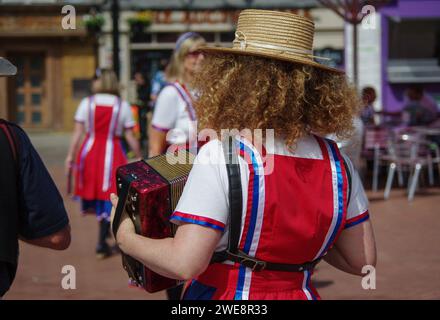 Morris Dancers putting on a display at a convention, Market Square, Northampton, UK; view of red haired lady accordion player Stock Photo