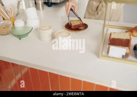 The waitress's hand puts the piece of cupcake on the table at a cafe standing behind bar counter Stock Photo