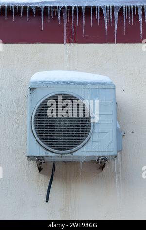 The conditioner covered with icicles on a yellow wall. Operation of the air conditioner in winter at low temperatures. Cooling, cold concept image. Stock Photo