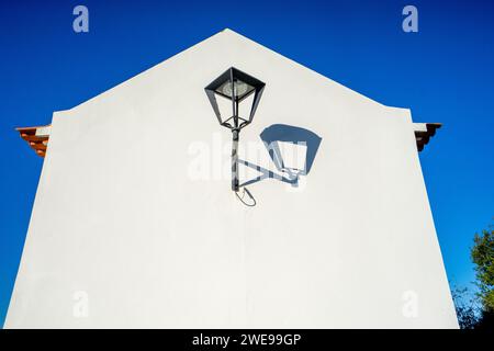 Old street lamp on a white wall against the blue sky, whith shadow Stock Photo