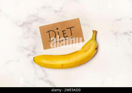 One banana with a diet sign on a white and gray marble kitchen counter in a top view Stock Photo