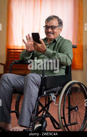 Vertical shot of happy elderly senior man with disability on wheelchair using mobile phone at home - concept of technology, social media and digital Stock Photo