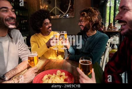Multiethnic group of four male friends gathering in a bar drinking beer and cheering celebrating. Stock Photo
