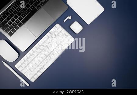 Top view of laptop computer, white keyboard, touchpad, mouse, earphones case and pen on dark blue background. Modern office flat lay, copy space. Stock Photo